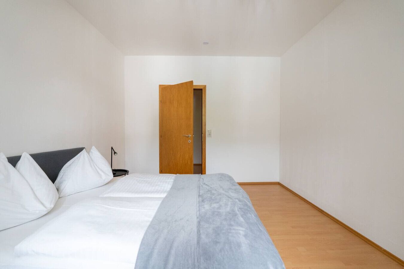 A bedroom with a bed, a desk, and a door leading to another room.