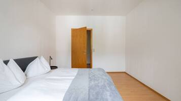A bedroom with a bed, a desk, and a door leading to another room.