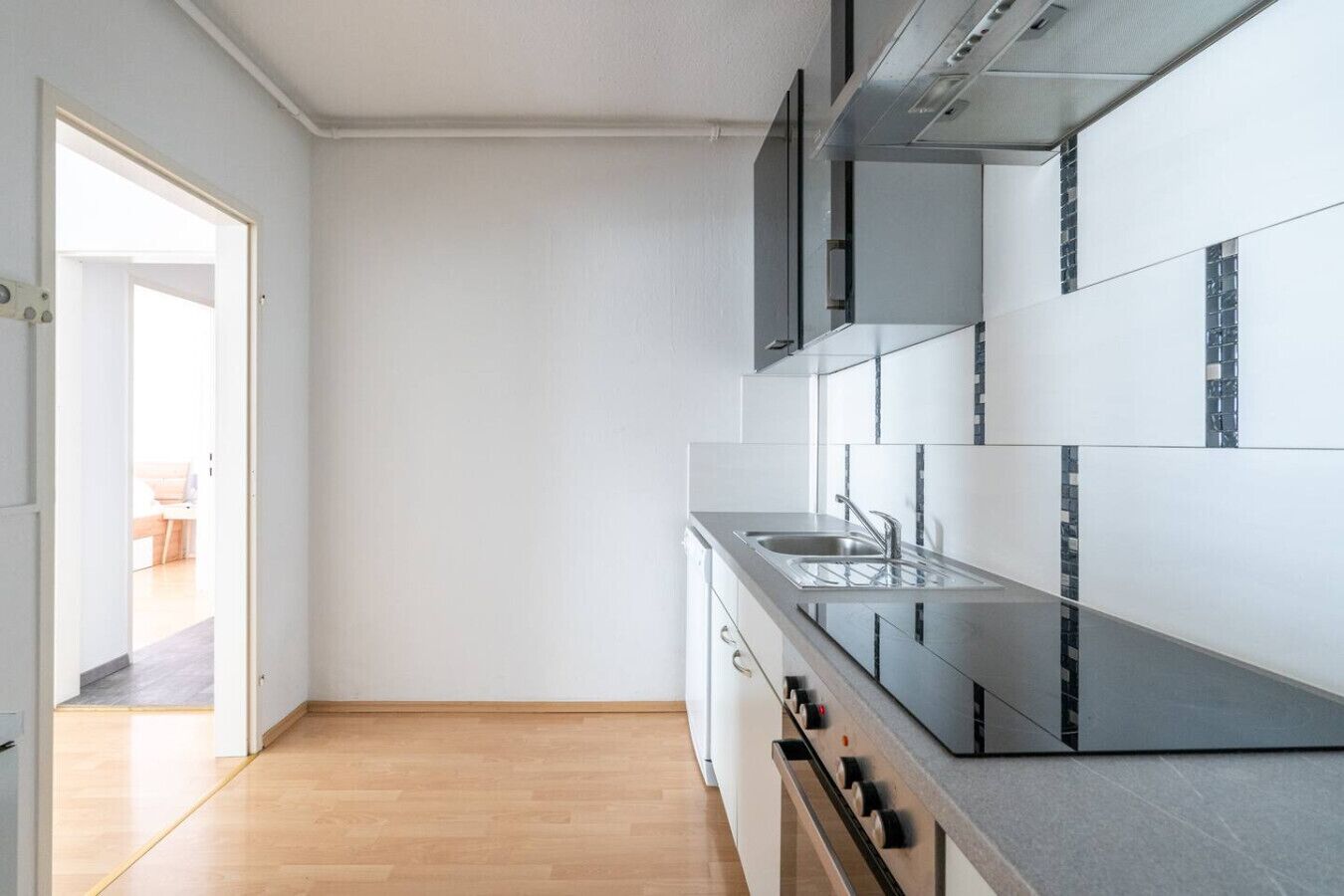 A modern kitchen with a stainless steel sink, a built-in oven, and a view into the adjacent living area.