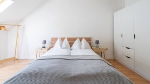 Une chambre à coucher comprenant un lit, deux tables de chevet, une armoire, un portant et un puits de lumière.