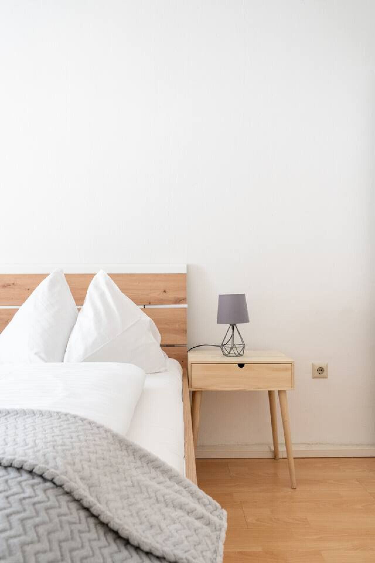 A bed with white bedding, a gray blanket, and a wooden headboard.