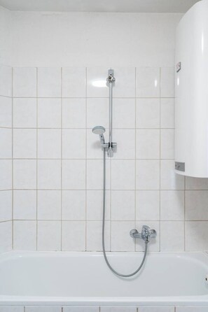 A bathroom with a bathtub, a showerhead, and a wall-mounted faucet.