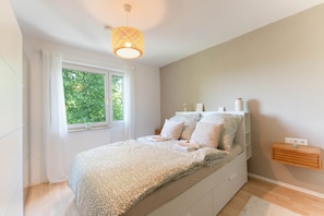 A bedroom with a bed, a window with curtains, a bedside table, and a hanging light fixture.