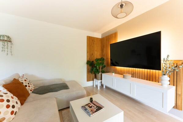 Una sala de estar moderna con un televisor de pantalla plana grande, un sofá, una mesa de centro y una planta.