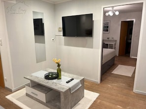 A modern bedroom with a bed, a TV mounted on the wall, a bedside table with a vase, and a wooden floor.