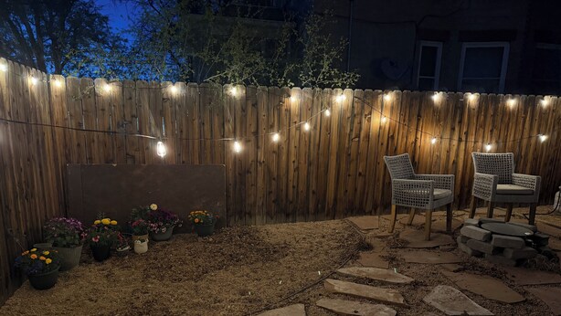A backyard with a wooden fence, potted plants, two wicker chairs, and a stone pathway.