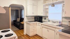 A compact kitchen with white cabinets, a microwave, a stove, and a window with a view.