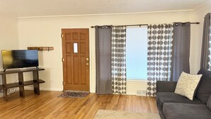 A living room with a wooden floor, a television on a stand, a sofa, and a door with curtains.