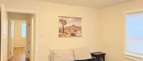 A bedroom with a bed, a nightstand, a window, and a desert landscape painting on the wall.