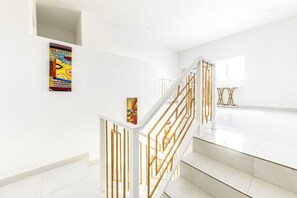 Eine Treppe mit weißen Wänden und goldenen Geländern, die zu einem hellen Raum mit einem großen Fenster führt.
