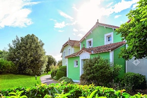 A green house with a tiled roof, surrounded by lush greenery and a clear sky. - Coast Home With Play Area (Talmont-Saint-Hilaire)