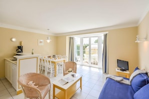 A living room with a sofa, a dining table with chairs, a kitchen area, and a TV on a small table. - Coast Home With Play Area (Talmont-Saint-Hilaire)