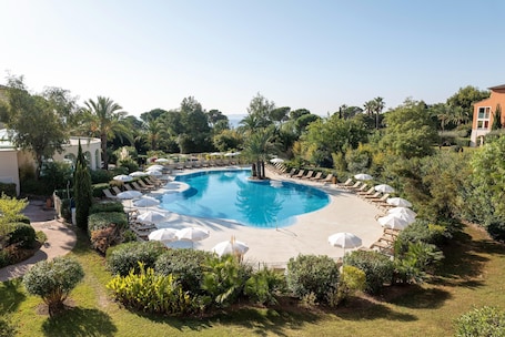 A circular pool with lounge chairs and umbrellas, surrounded by greenery and a clear sky.. Picturesque 4-person Seaside Retreat