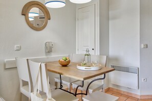 Un comedor con una mesa de madera, sillas blancas, un cuenco de fruta, una jarra de vidrio y una bandeja blanca.
