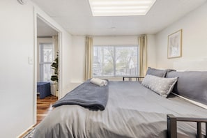 Un dormitorio con cama, ventana, planta y puerta.