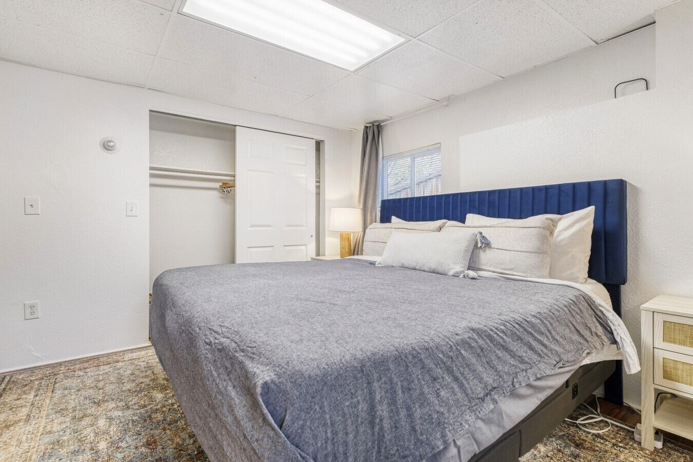 A bedroom with a bed, a nightstand, a window, and a door.