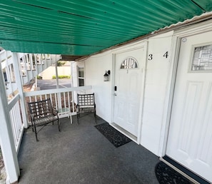 Eine überdachte Veranda mit zwei Stühlen, einem kleinen Tisch und einer weißen Tür mit der Nummer 34.