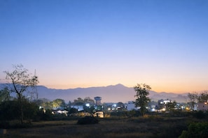 A cityscape at dusk with buildings, a water tower, and mountains in the background. - Sunrise Haven - Peaceful Retreat Near Rishikesh (Raiwala)