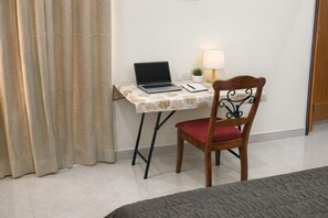 A room with a bed, a desk with a laptop, a chair, a lamp, and a curtain.