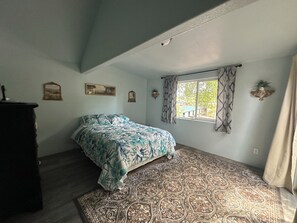 A bedroom with a bed, a window with curtains, a patterned rug, and wall-mounted decor.