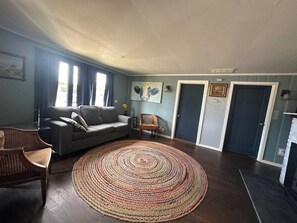 A living room with a grey sofa, a round rug, a wicker chair, and a door.