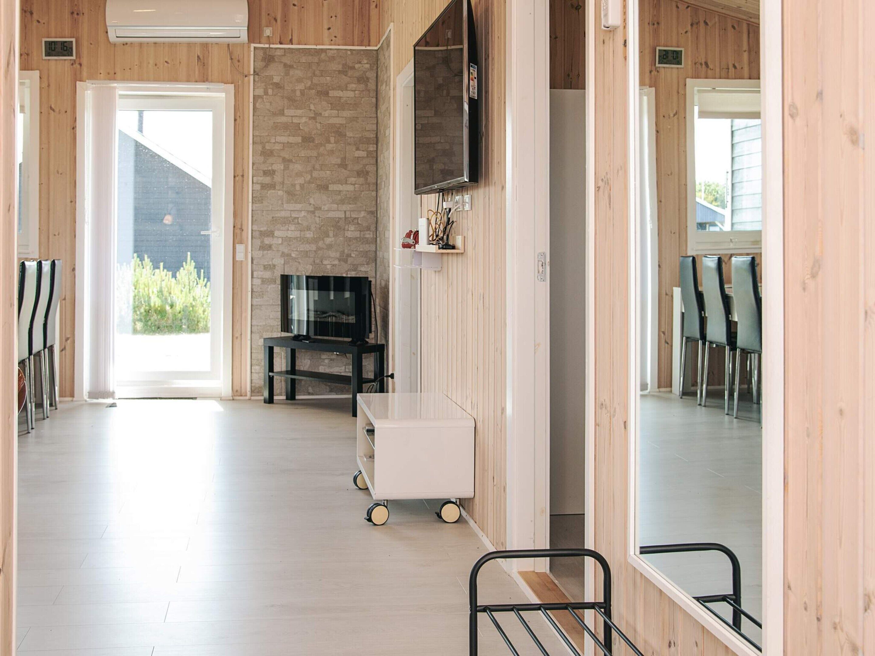 Un intérieur moderne avec un mur en pierre, un téléviseur fixé au mur, un chariot à roulettes et un coin repas avec des chaises.