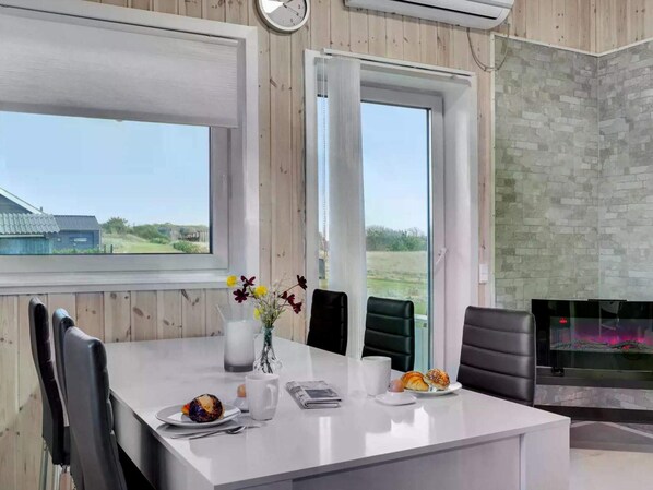 Ein modernes Zimmer mit einem großen Fenster, einem Kamin und einem Esstisch mit Frühstücksgebäck.