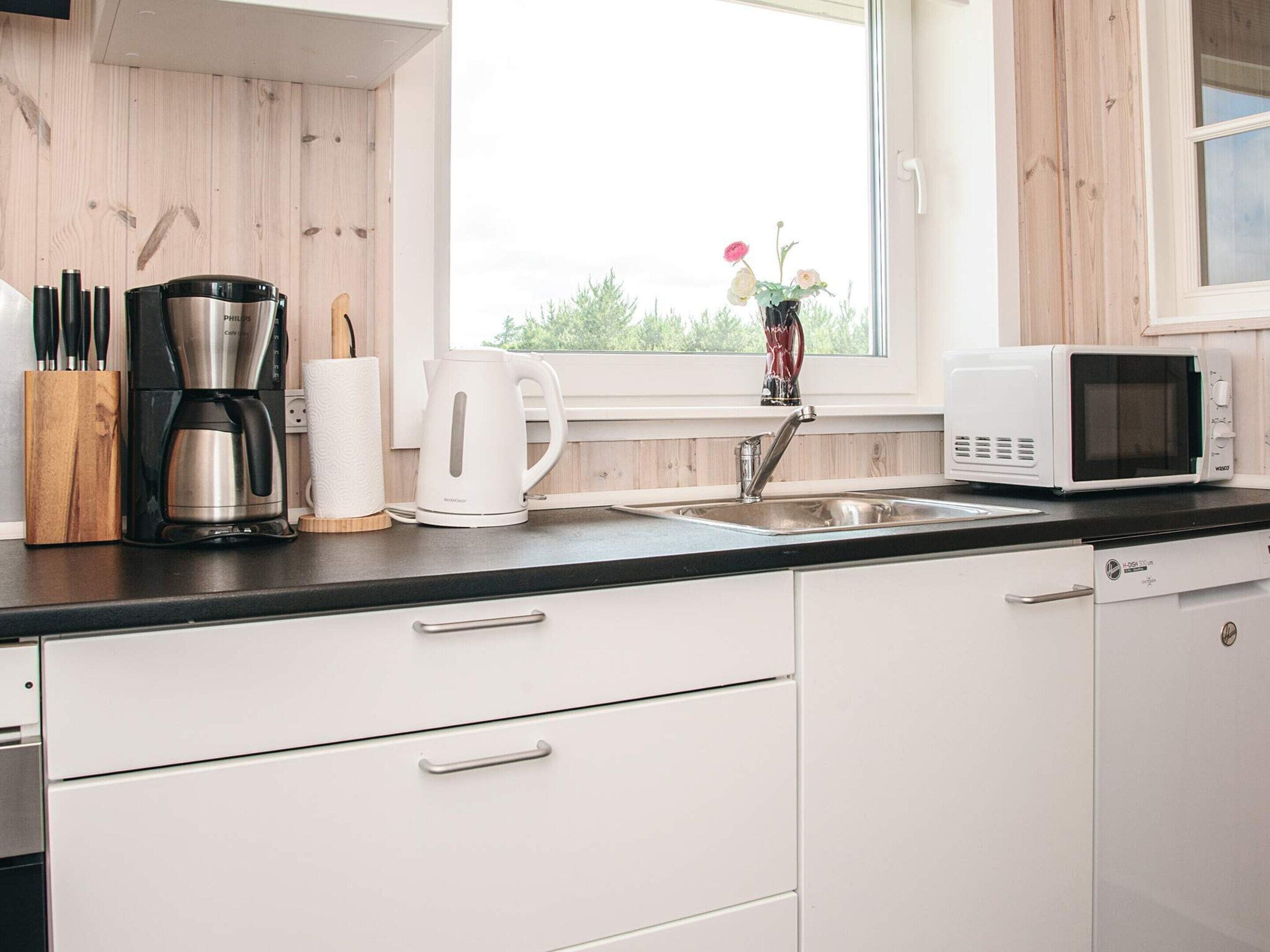 A modern kitchen with a coffee maker, kettle, microwave, and a sink.
