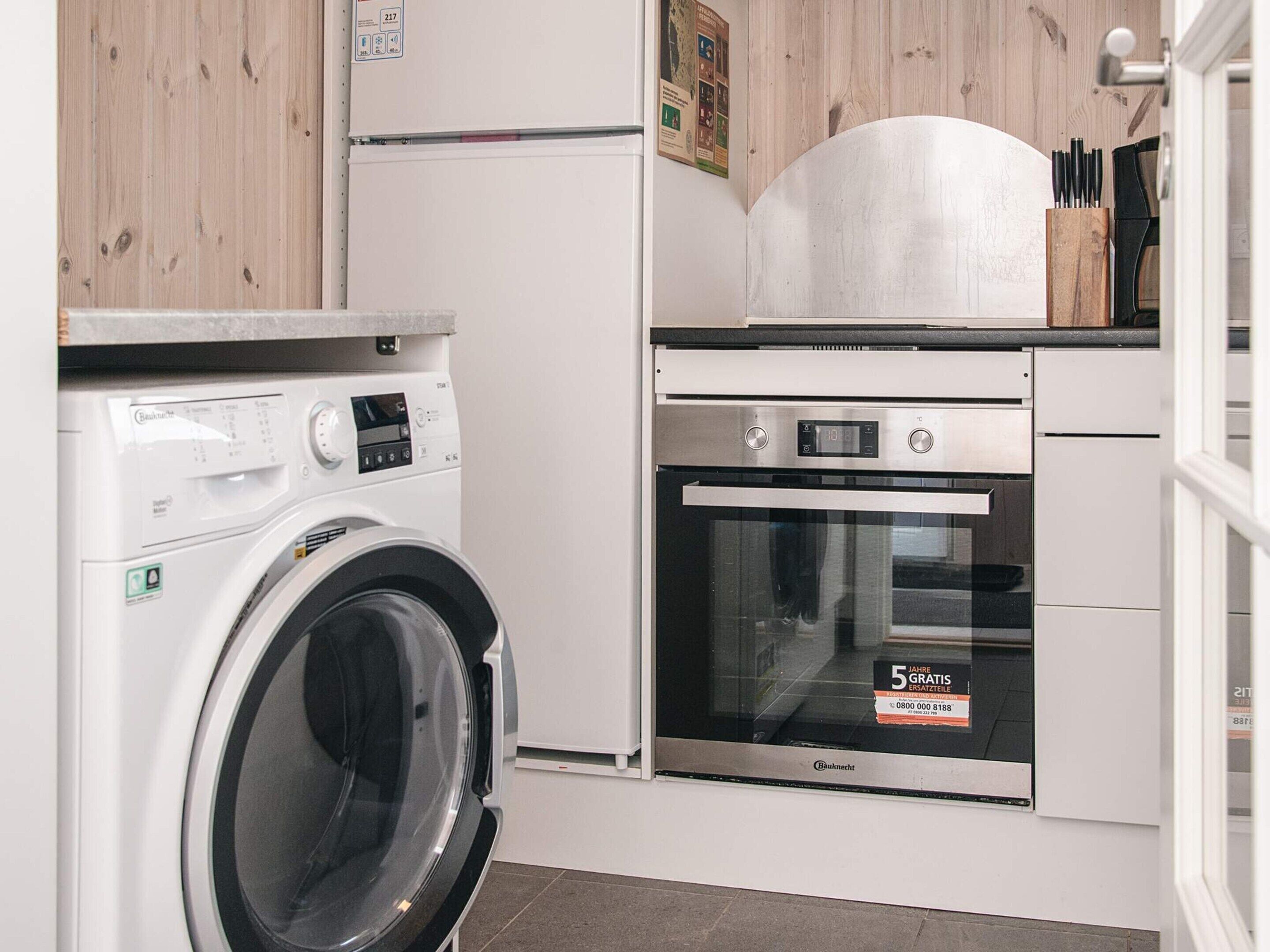 Un espace buanderie équipé d’un lave-linge à chargement frontal et d’un four encastré.