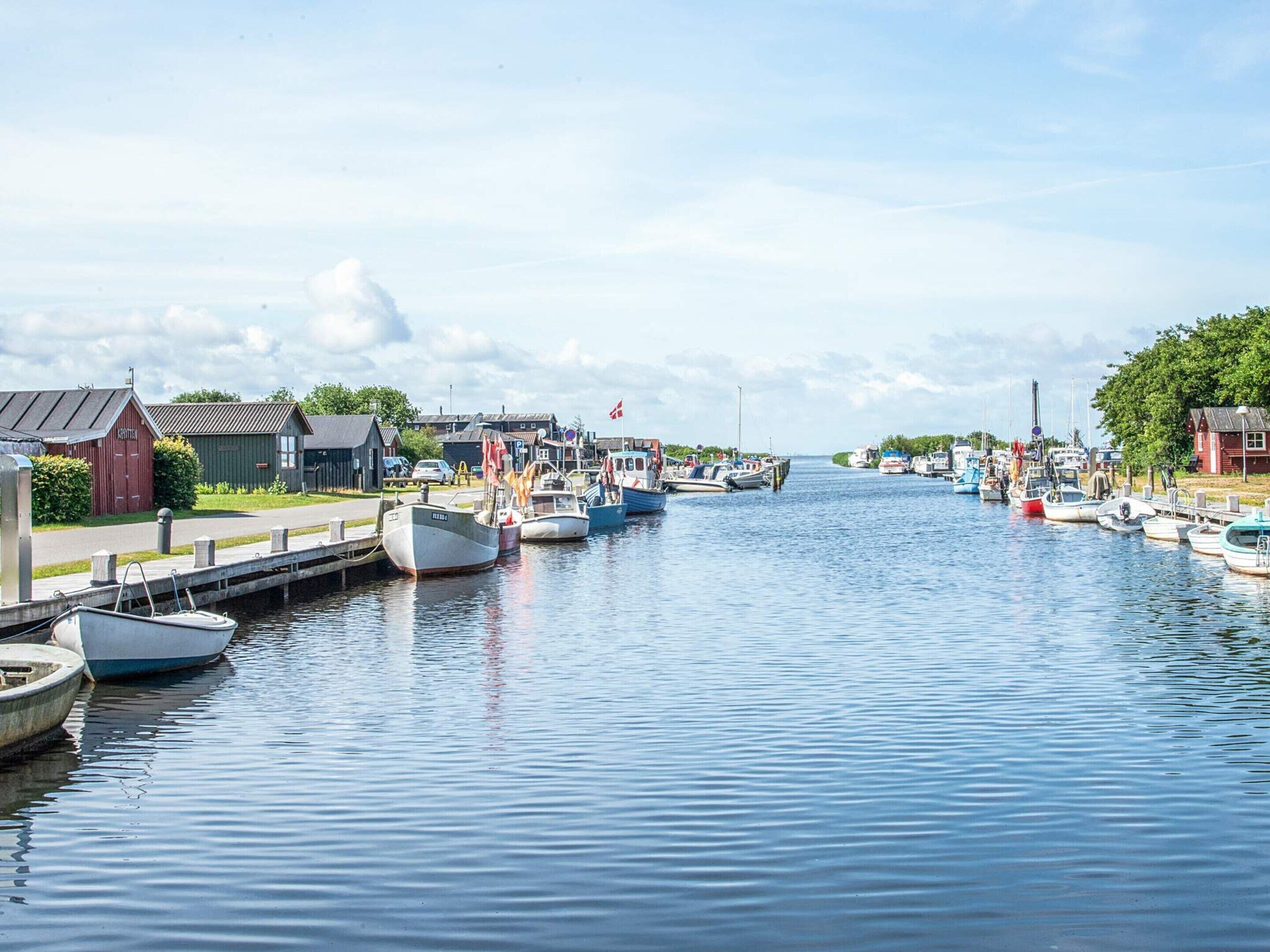 A calm waterway with boats docked on both sides, a red building with a sign, and a clear sky.