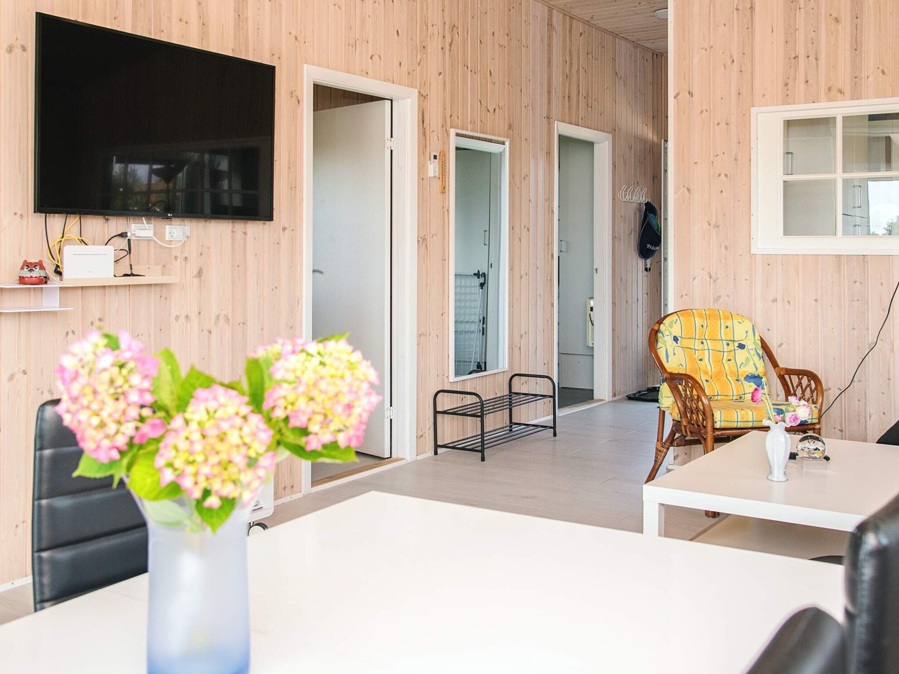 A modern living room with a flat-screen TV, a dining table, and a wicker chair.
