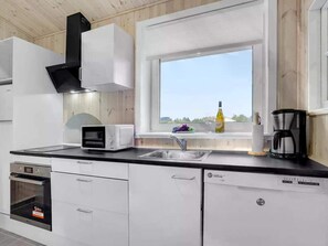 Eine moderne Küche mit Einbauofen, Mikrowelle und Geschirrspüler, ein Fenster mit Blick und eine Kaffeemaschine auf der Arbeitsfläche.
