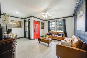 A living room with a red door, a ceiling fan, a sofa with star-patterned pillows, and a coffee table. - Newly updated Home with Pool, Patio, BBQ! 5BR 3BA 10mi from Downtown Sleeps 15 (Houston)