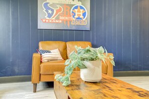 A room with a brown leather sofa, a wooden coffee table, and a potted plant. A wall-mounted sign displays the Houston Rockets and Astros logos. - Newly updated Home with Pool, Patio, BBQ! 5BR 3BA 10mi from Downtown Sleeps 15 (Houston)