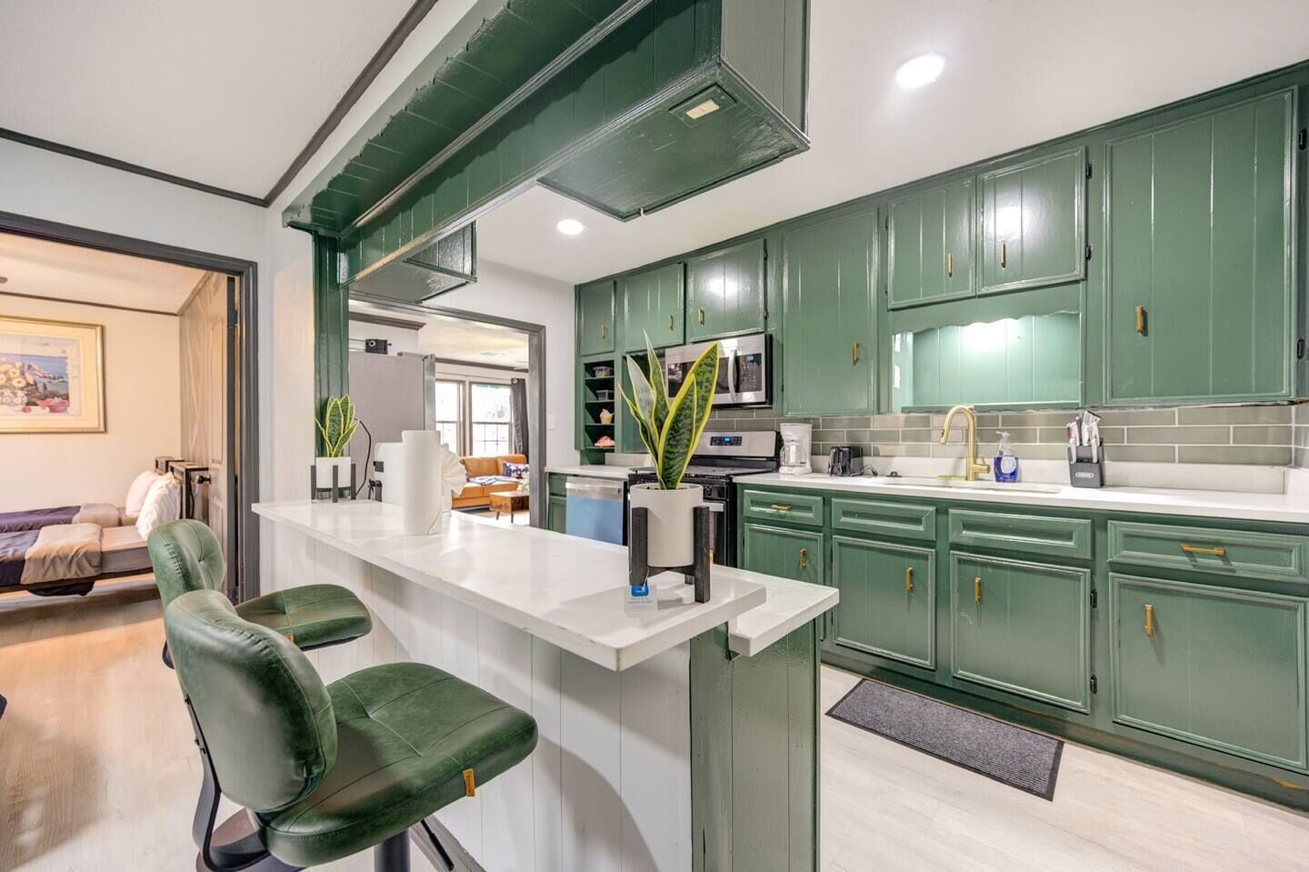 Une cuisine moderne avec des meubles verts, un plan de travail blanc et un coin bar avec des chaises vertes.