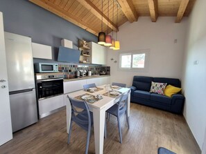 A compact kitchen with modern appliances, a dining table set for four, and a blue sofa in a bright living area. - Apartment in Villa with garden and private terrace (Kaukana)