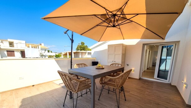Eine Dachterrasse mit Tisch, Stühlen und einem großen Sonnenschirm, mit Blick auf die umliegenden Gebäude.