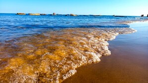 Ein Strand mit klarem Wasser, sandigem Ufer und fernen Felsenformationen.