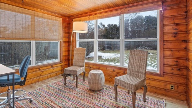 Et interiør af en bjælkehytte med store vinduer, fletstole, et bord og en farverig måtte.