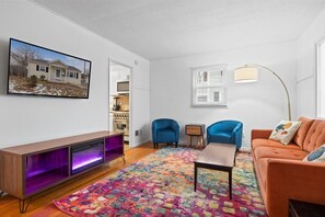 A living room with a TV, sofa, chairs, a colorful rug, and a fireplace.