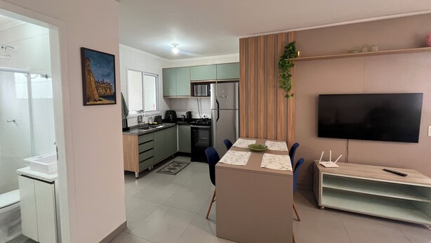 A modern kitchen with a dining area, a flat-screen TV, and a small island. - New and Cozy - near SESC (Bertioga)