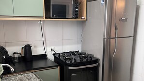 A kitchen with a microwave, stove, refrigerator, granite countertop, and a sink. - New and Cozy - near SESC (Bertioga)