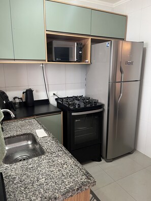 A kitchen with a microwave, stove, refrigerator, granite countertop, and a sink.