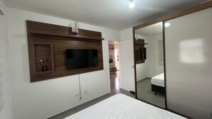 A bedroom with a bed, a TV mounted on the wall, and a mirror. - New and Cozy - near SESC (Bertioga)