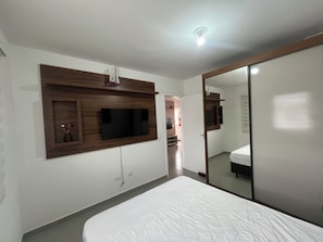 A bedroom with a bed, a TV mounted on the wall, and a mirror.