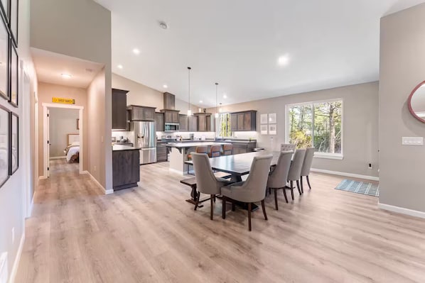 A modern kitchen with a central island, dining area with chairs, and a visible door leading to a bedroom.