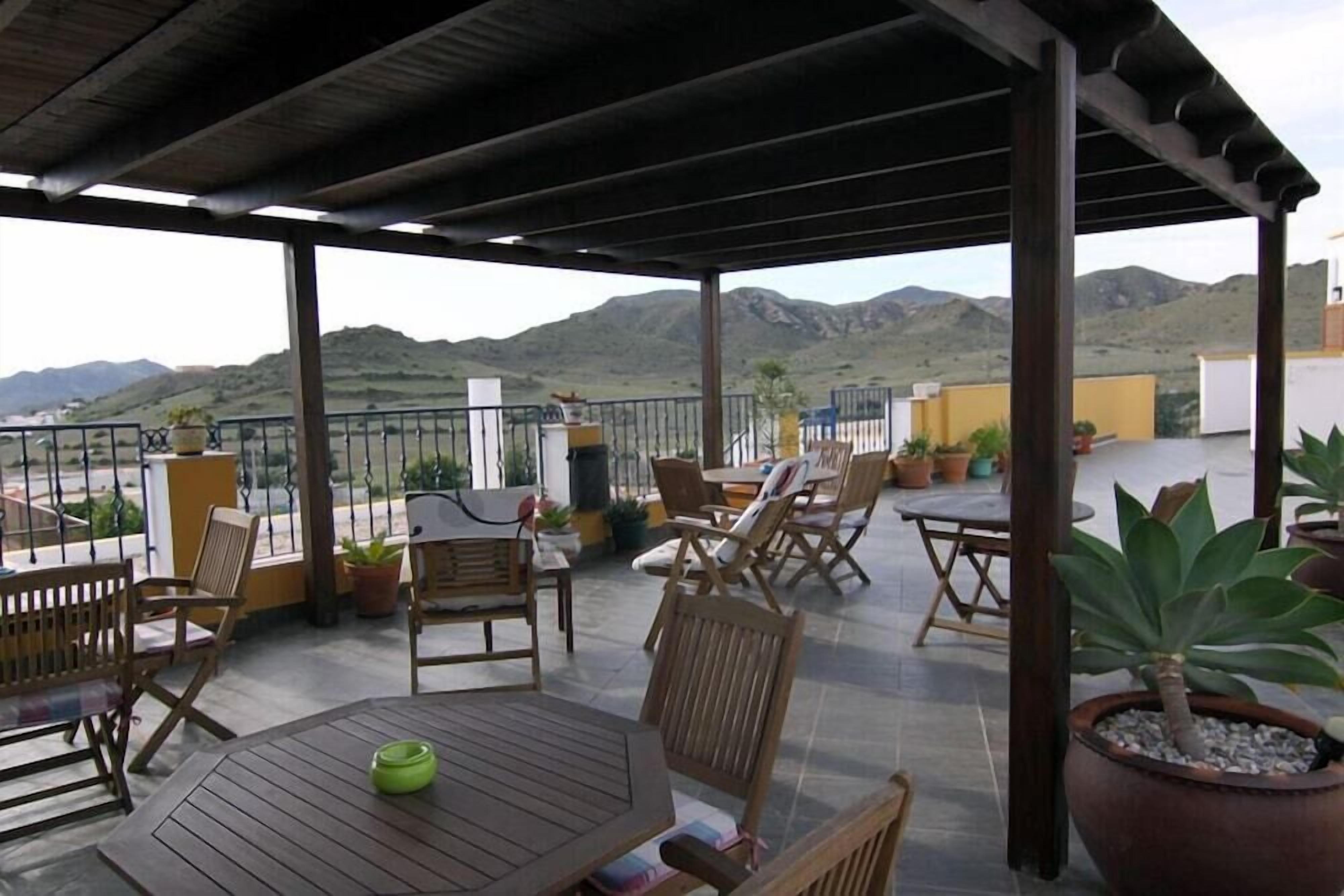 An outdoor patio with wooden furniture, potted plants, and a view of mountains.