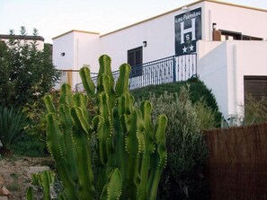 Un edificio con un cartel que dice 'Los Palmitos Hs' y un cactus grande al frente.