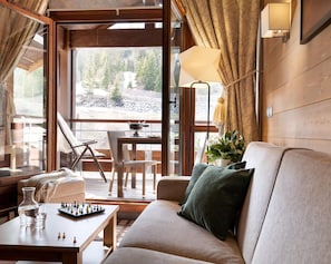Una habitación acogedora con un sofá, una mesa con un tablero de ajedrez, una lámpara y vistas a un área boscosa.