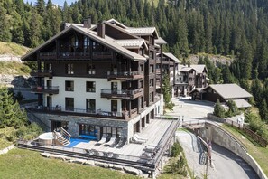 Un hotel de varios pisos con balcones, una zona de piscina y montañas al fondo.